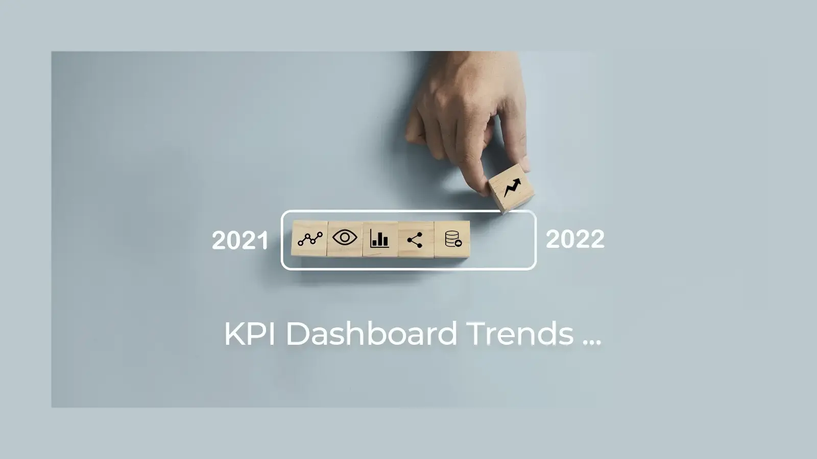 Hand placing pieces of wood with dashboard icons etched on them in a row. The words KPI Dashboard trends 2022 are written in white on the background.