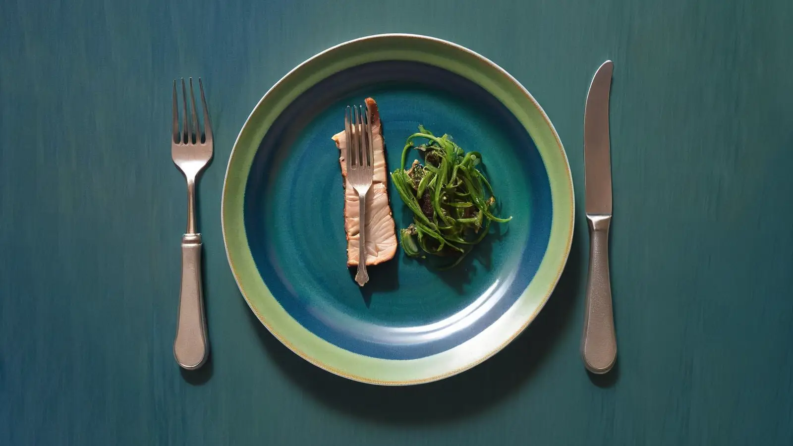 Tiny steak meal on a blue and green plate with a knife and fork on either side